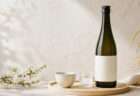 生成り色の空間に日本酒の四合瓶と酒器を配した写真