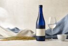 生成り色と藍色の空間に紺色の日本酒瓶と酒器を配した写真