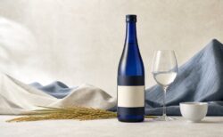 生成り色と藍色の空間に紺色の日本酒瓶と酒器を配した写真