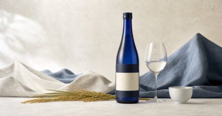 生成り色と藍色の空間に紺色の日本酒瓶と酒器を配した写真