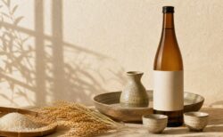 生成り色の空間に日本酒瓶と燗酒器、稲穂を配した写真